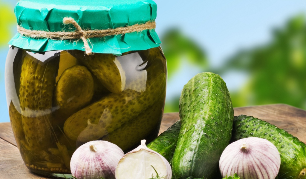 Консервированные огурцы в банке на столе со свежими огурцами и чесноком