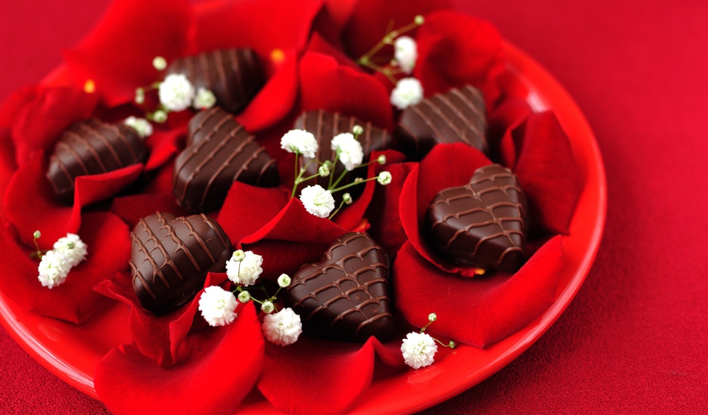 Шоколадные конфеты в форме сердца на тарелке с лепестками розы
