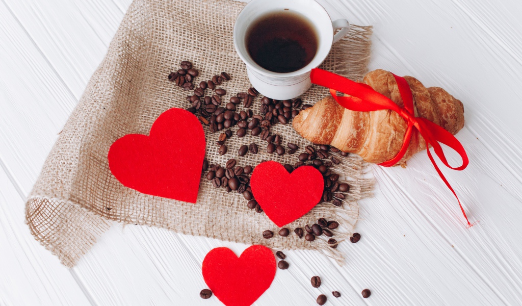 Круассан с чашкой кофе и кофейными зернами на столе с красными сердечками