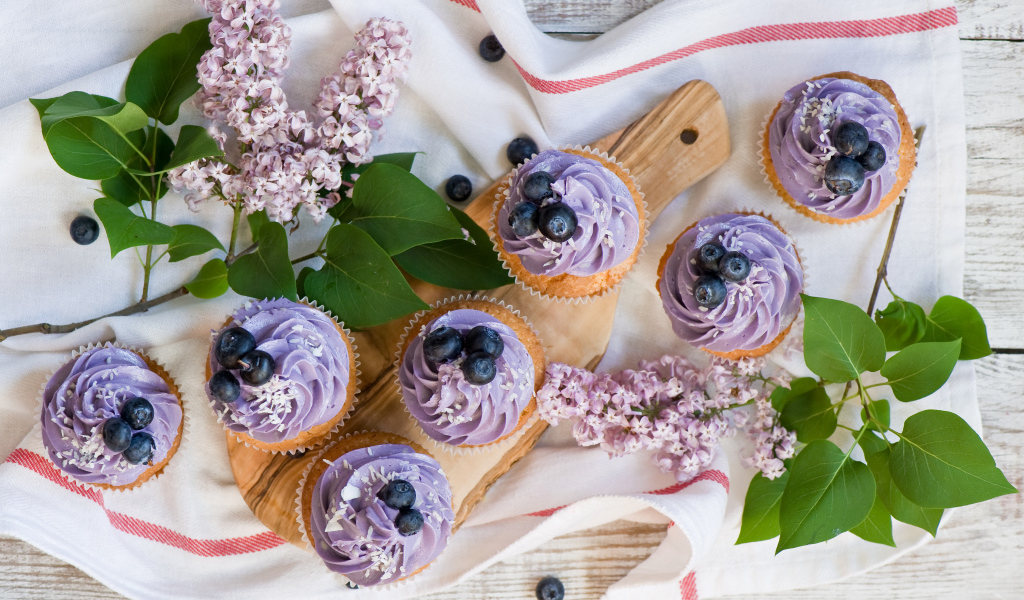 Кексы с кремом и ягодами черники на столе с ветками сирени 
