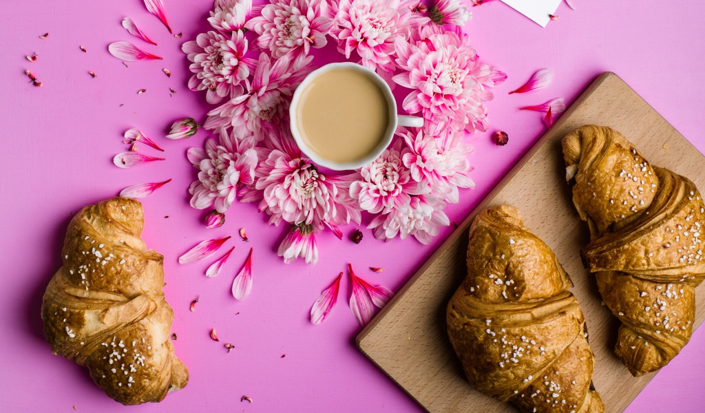 Свежие круассаны на столе с чашкой какао и цветами хризантемы