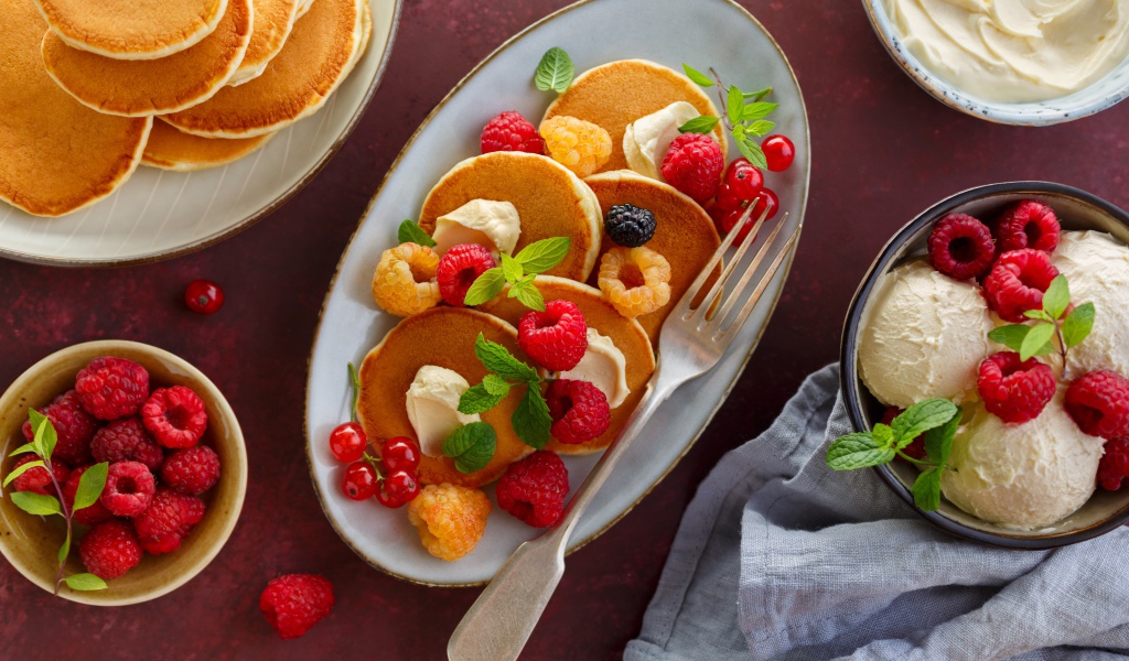 Оладьи на столе с ягодами малины и мороженым