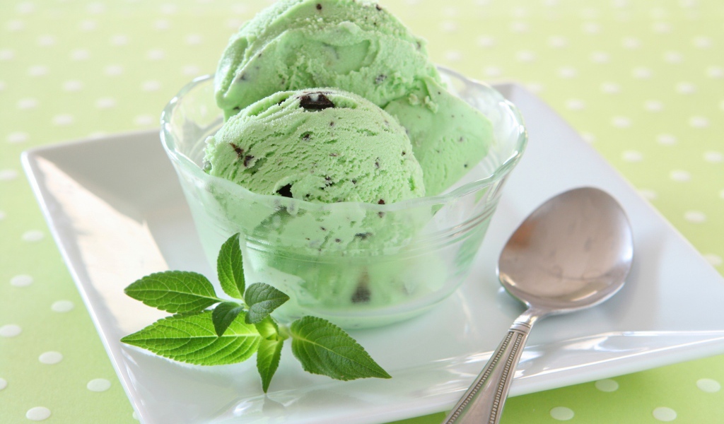 Зеленые шарики мороженого с шоколадом и мятой на тарелке с ложкой