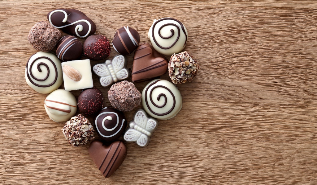 Сердце из шоколадных конфет ассорти на деревянном столе