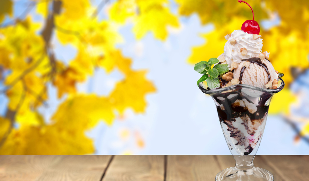 Мороженое в креманке с вишенкой на фоне желтых листьев