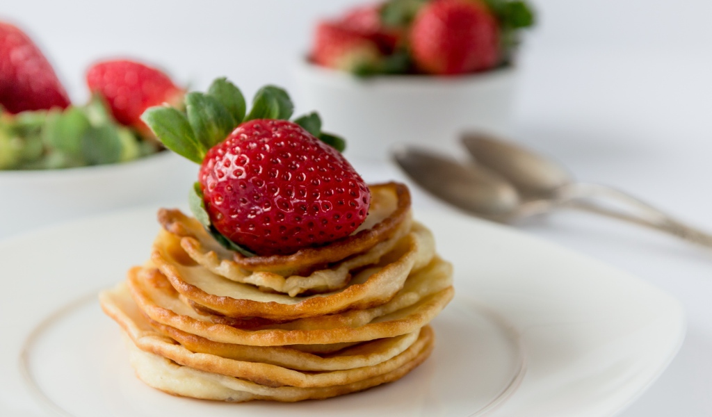 Оладьи с ягодами свежей клубники на белой тарелке 