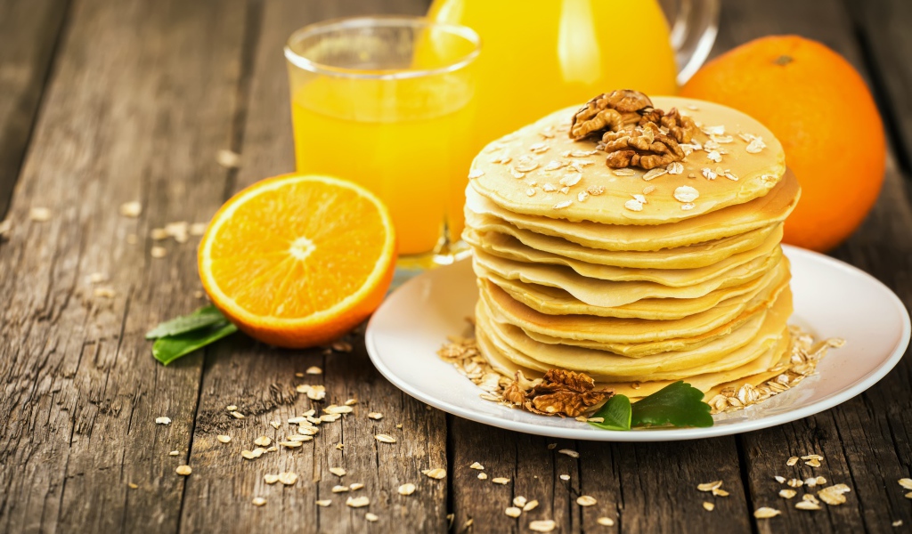 Оладьи с орехами на столе с апельсиновым соком и апельсинами