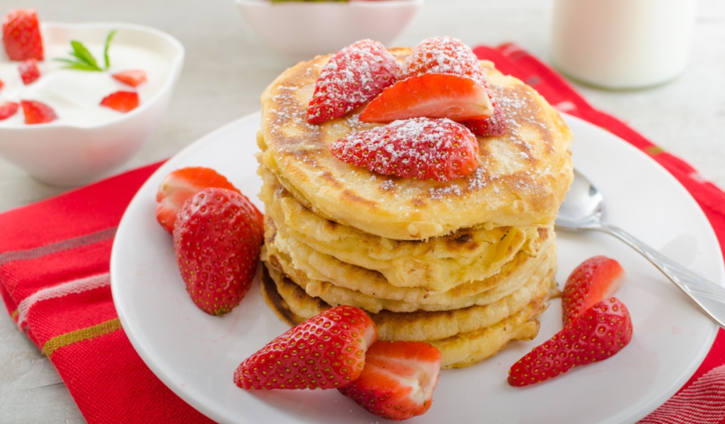 Оладьи с клубникой и сахарной пудрой на белой тарелке 