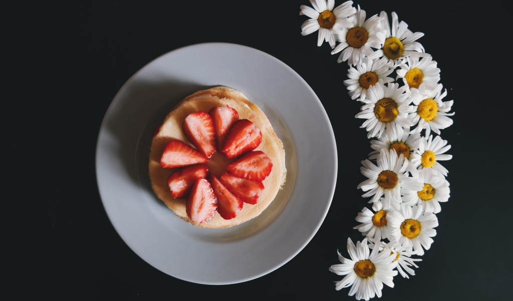 Оладьи с клубникой на тарелке на сером фоне с ромашками