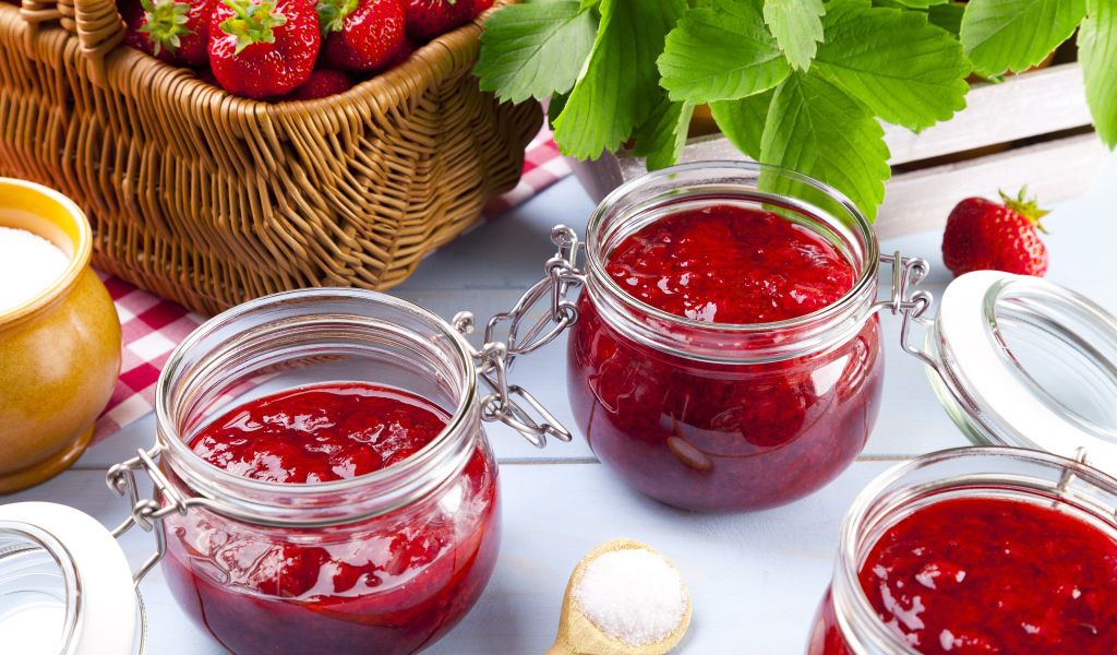 Клубничное варенье в стеклянных баночках на столе  ягодами