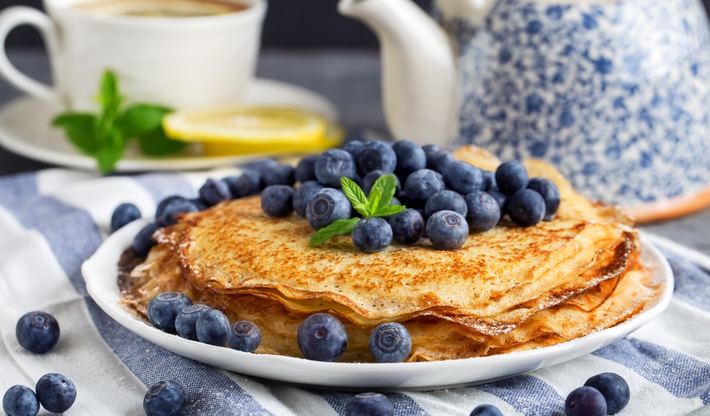 Тонкие блины с ягодами черники на столе с чаем