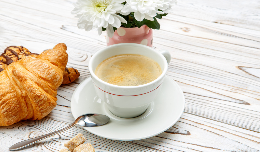 Чашка кофе и круассаны на столе с белыми хризантемами 