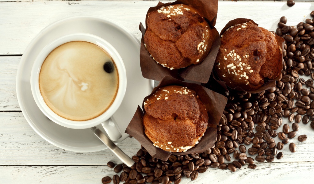 Чашка кофе с кексами и кофейными зернами на столе