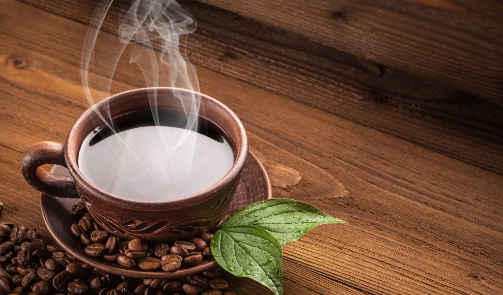 Чашка горячего кофе с зернами на деревянном столе