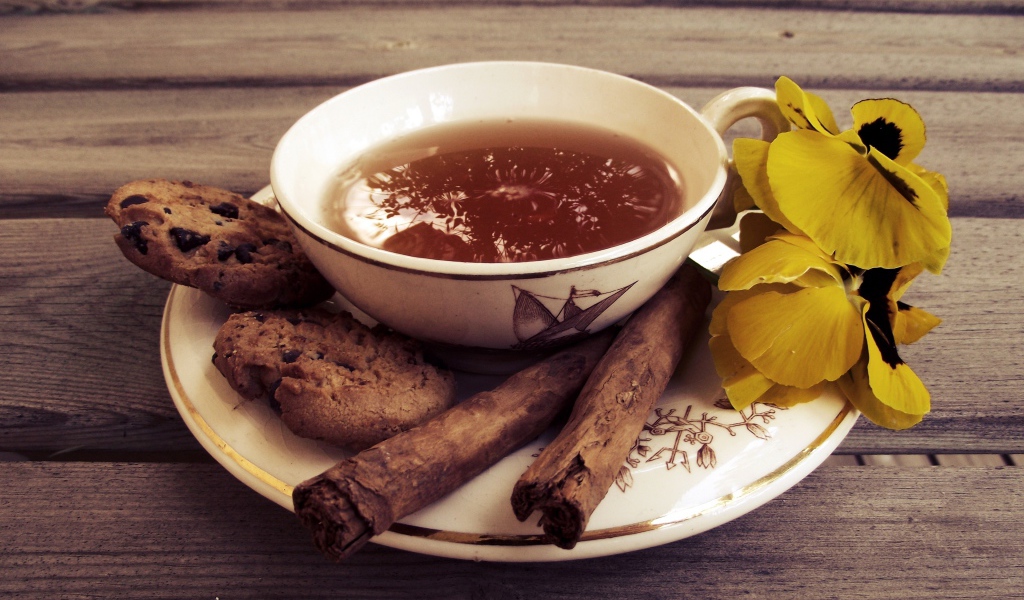 Чашка чая с печеньем, палочками корицы и цветами 