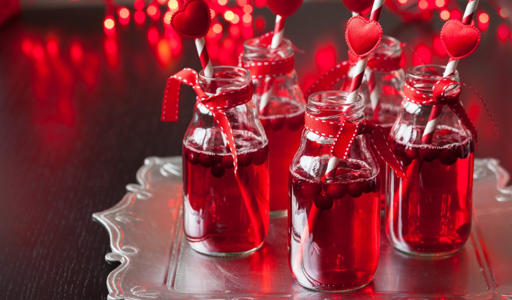 Вкусный напиток с клюквой в стеклянных бутылках на столе с трубочками