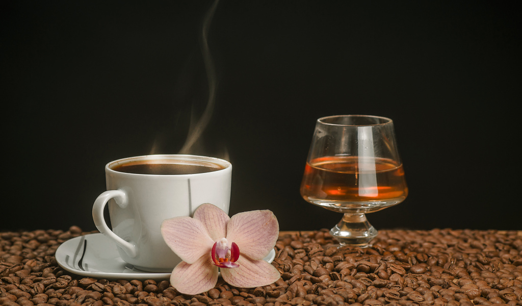 Ароматная чашка кофе на столе с бокалом виски, кофейными зернами и цветком орхидеи