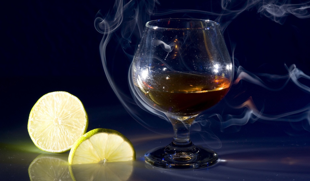 Бокал коньяка в дыму с кусочками лимона