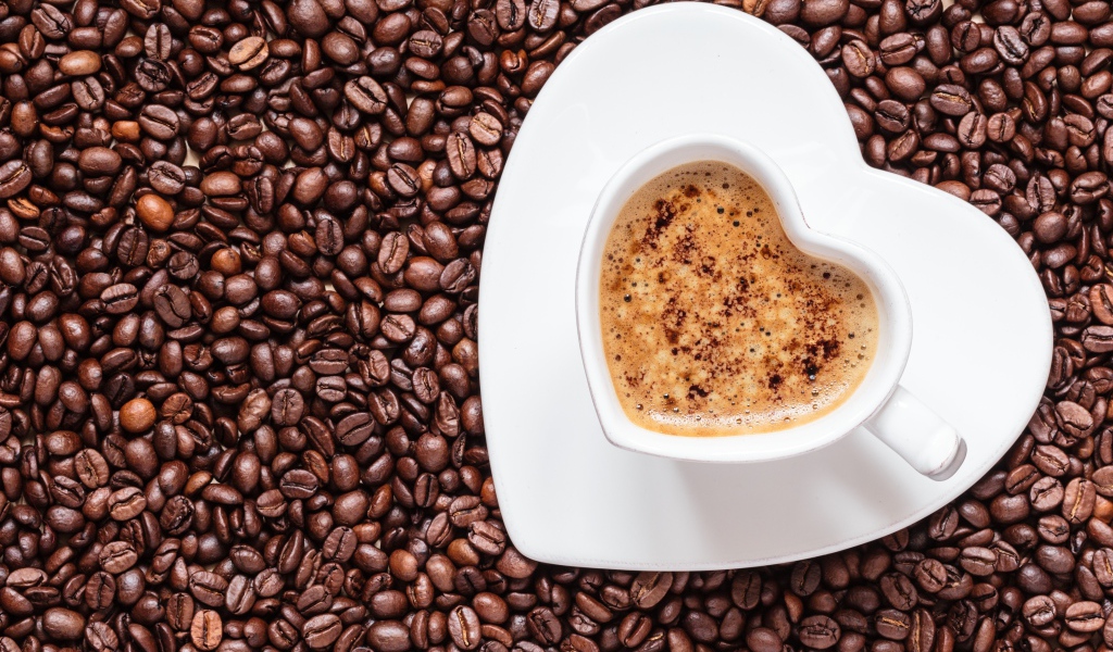 Белая чашка кофе в форме сердца стоит на кофейных зернах