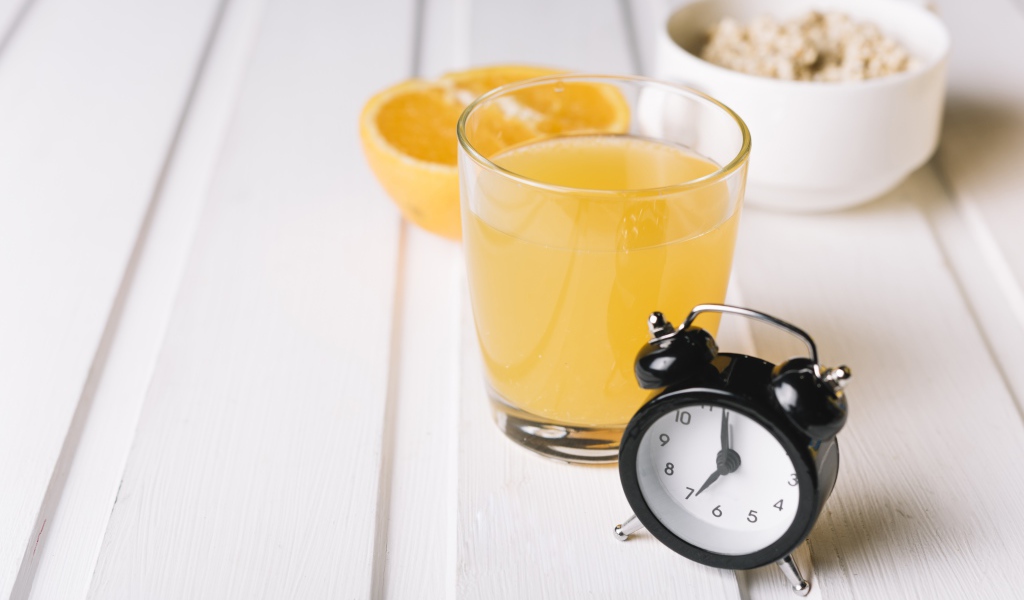 Черный будильник на столе со стаканом сока и хлопьями 