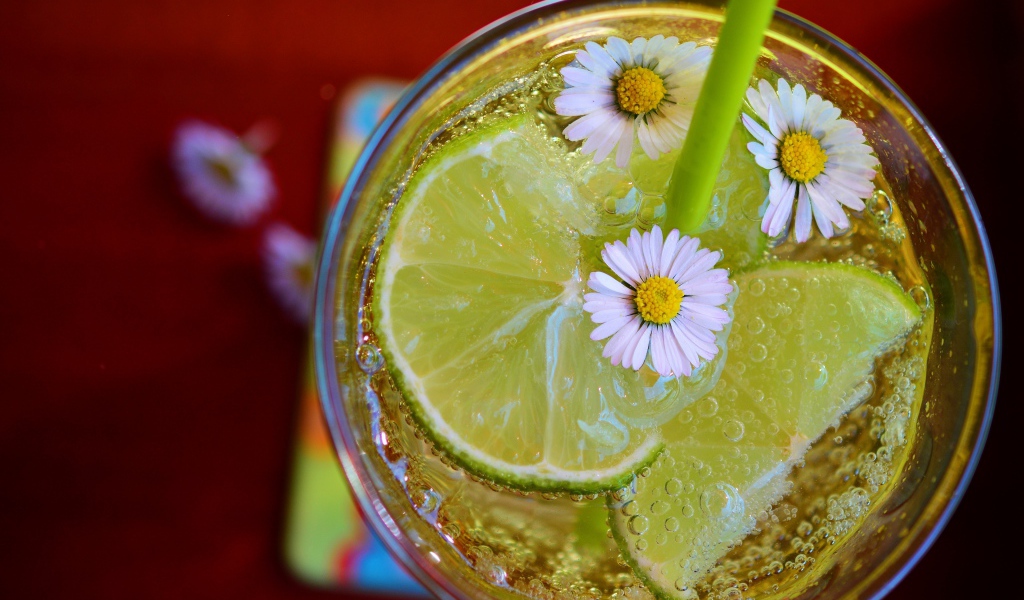 Газированный напиток с кусочками лайма и ромашками в стакане 