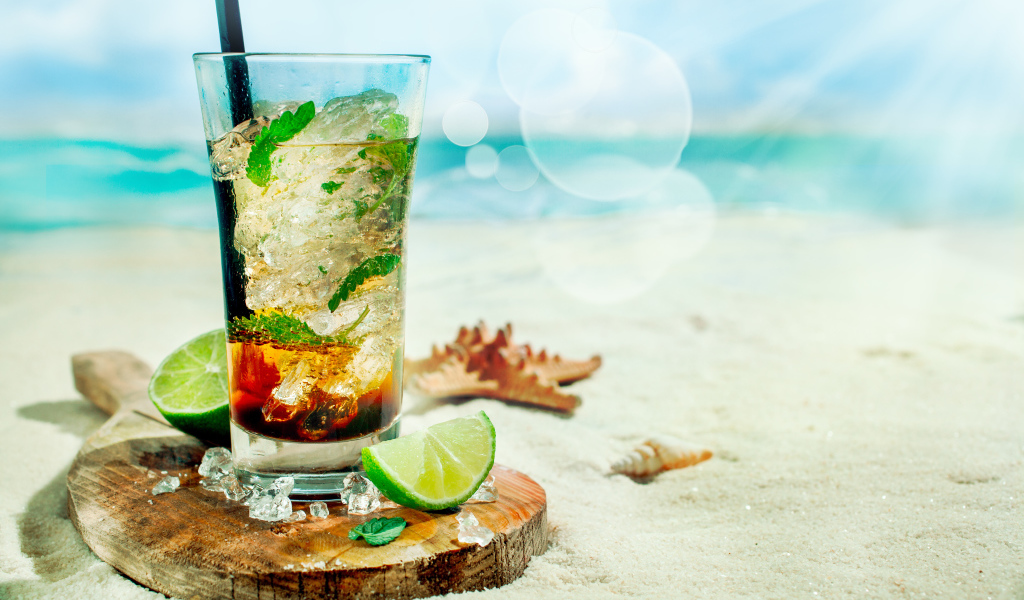 Коктейль в стакане с лаймом и кубиками льда стоит на песке на пляже