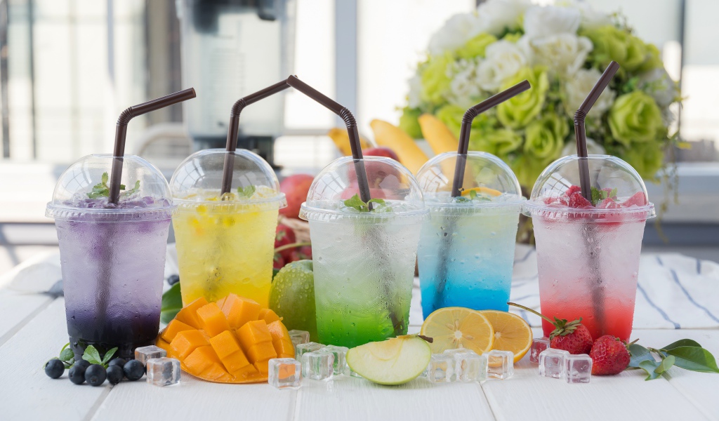 Коктейли в стаканах с трубочками на столе с кубиками льда и фруктами