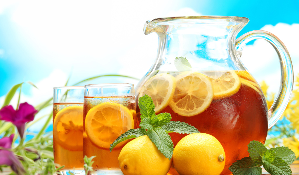 Холодный лимонад в графине на столе со стаканами и плодами лимона