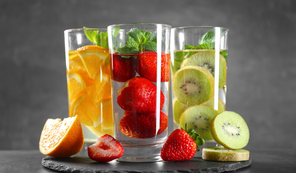 Напитки в стаканах с клубникой, киви и апельсинами на сером фоне