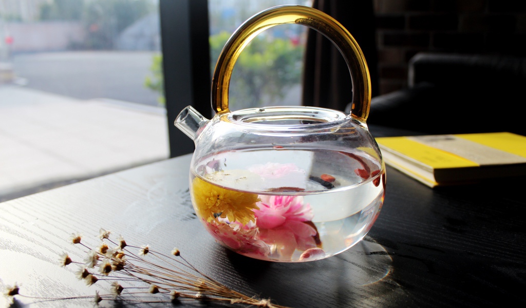 Цветочный чай в стеклянном чайнике на столе 