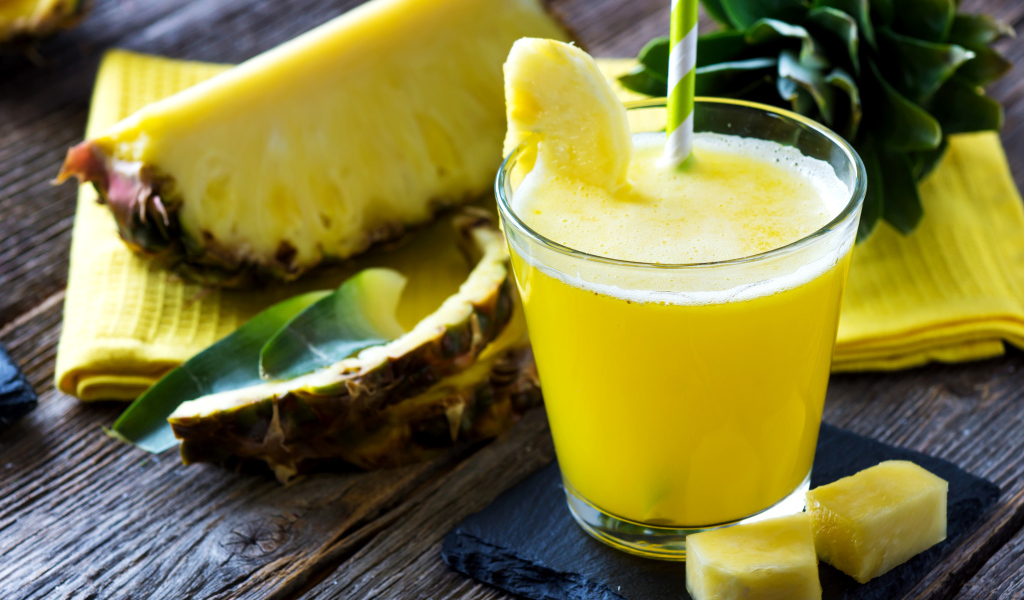 Ананасовый напиток в стакане на столе со свежими ананасами
