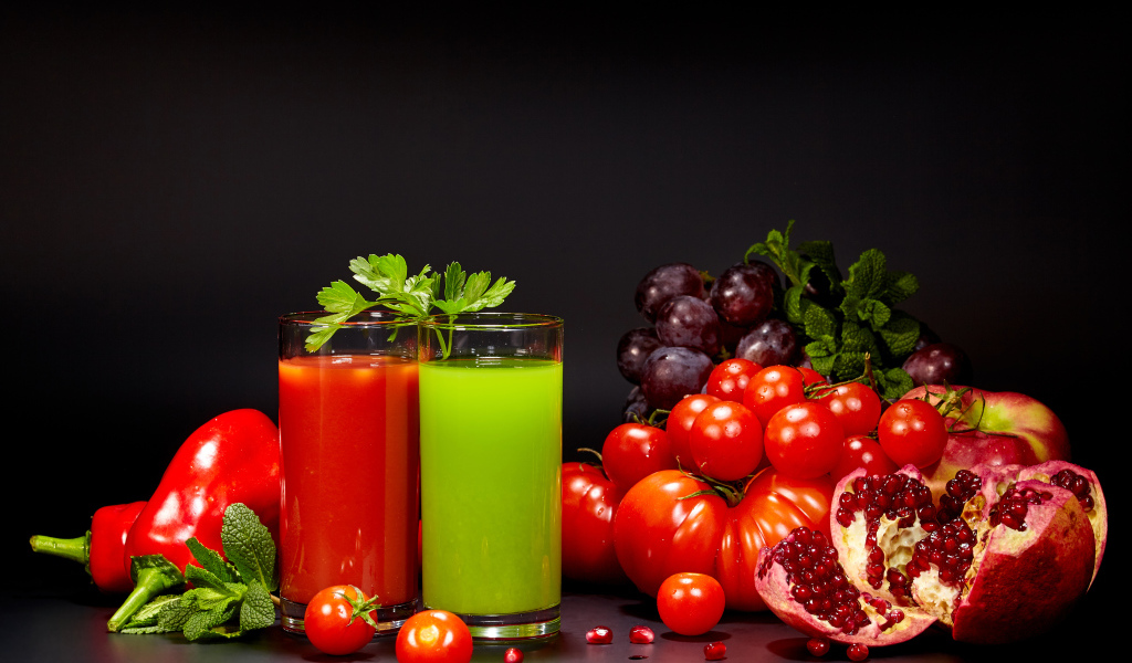 Два стакана сока на столе со свежими помидорами, перцем, гранатом, виноградом и зеленью