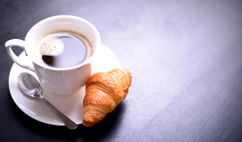 White cup of coffee on a table with a croissant