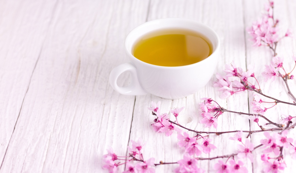 Белая чашка зеленого чая на столе с розовыми цветами