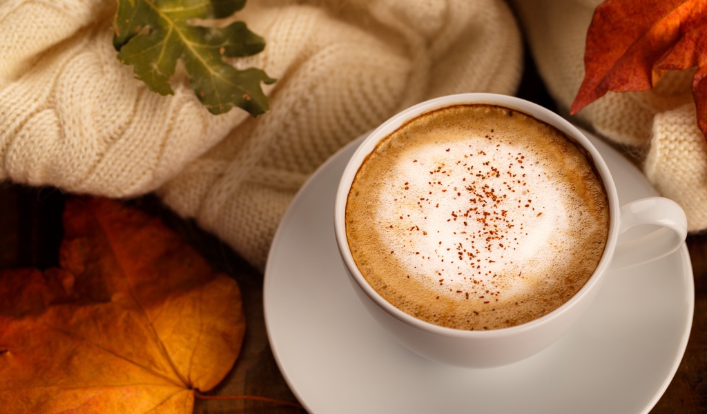 Белая чашка с вкусным кофе на столе с желтыми листьями