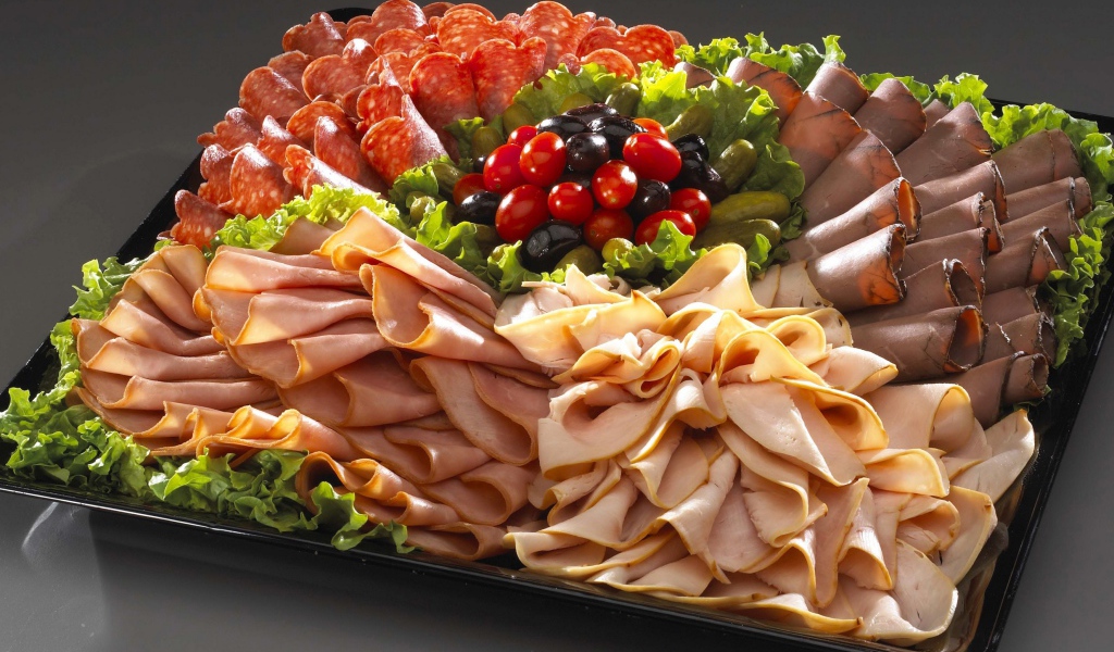 Большое блюдо с аппетитной мясной нарезкой, листьями салата и оливками