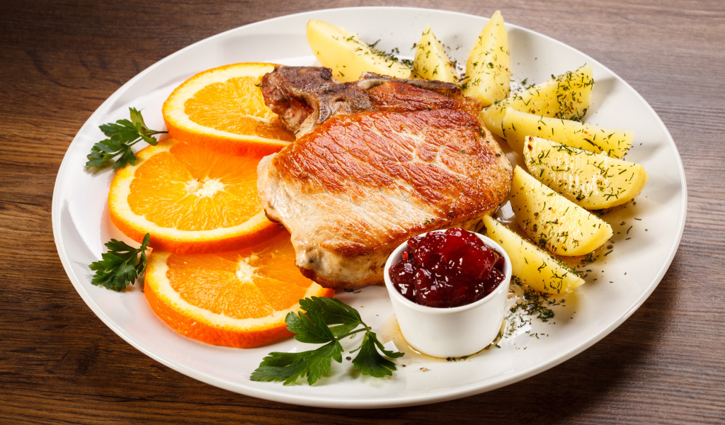 Кусок запеченного мяса с кусочками картофеля и апельсина и соусом