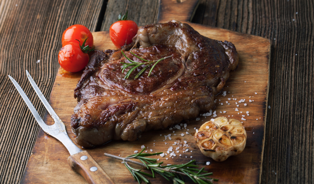 Кусок жареного мяса на разделочной доске с помидорами и чесноком