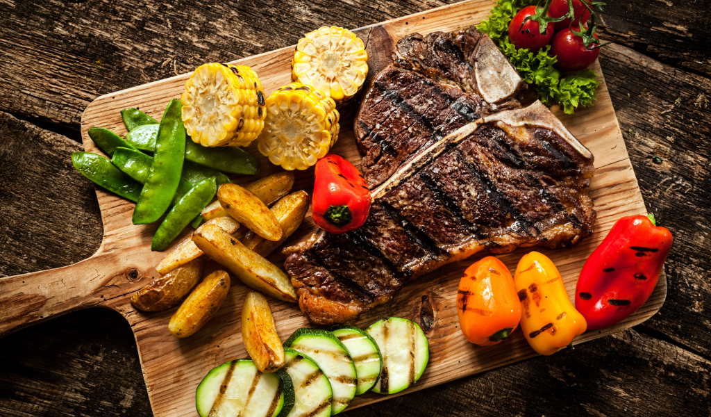 Кусок мяса на разделочной доске с овощами