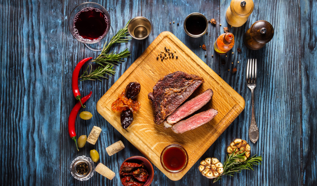 Кусок мяса на столе со специями и стаканом вина