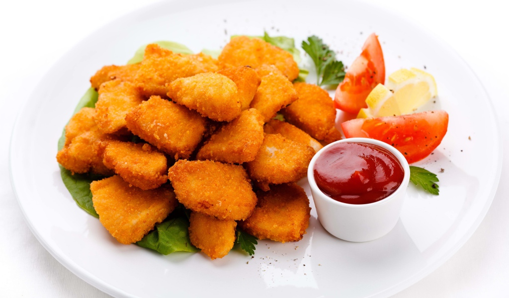 Куриные наггетсы с соусом и помидорами на белой тарелке 
