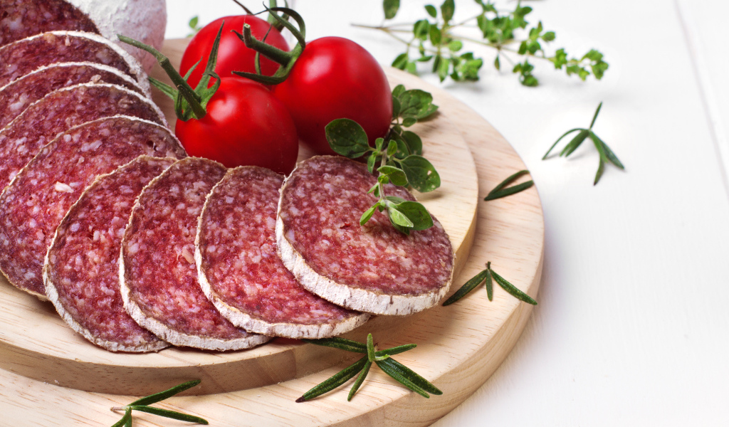 Вкусная колбаса на разделочной доске с помидорами и зеленью 