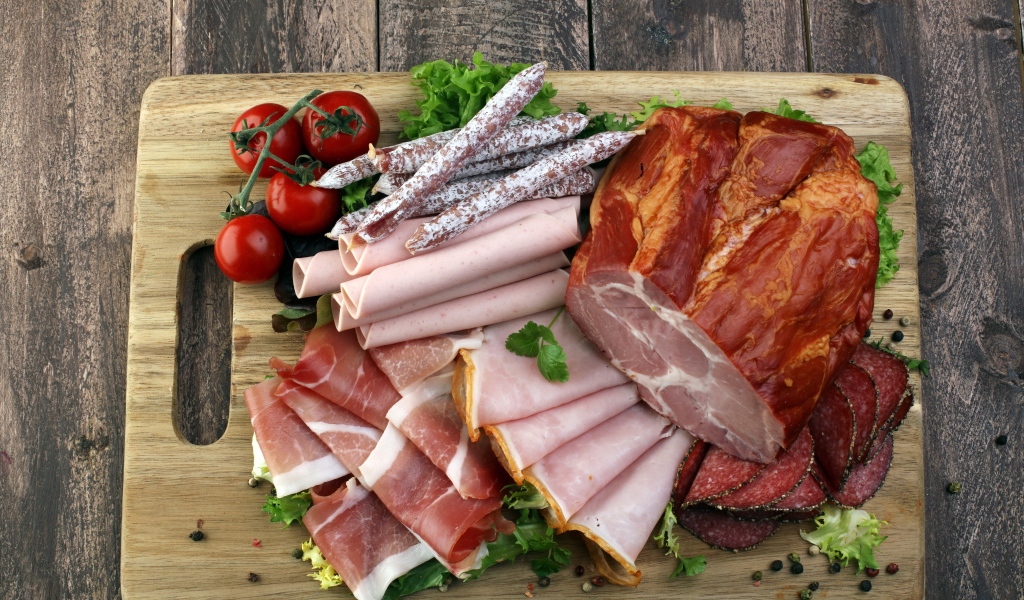 Мясная нарезка на разделочной доске с помидорами