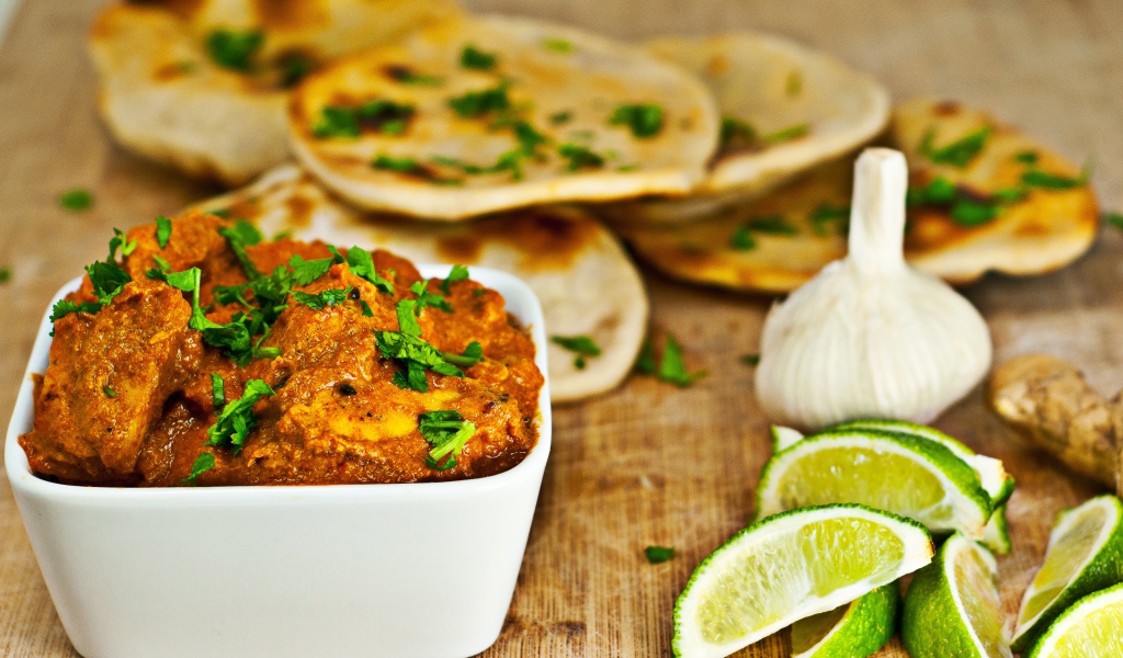 Мясное блюдо на столе с лепешками, кусочками лайма и чесноком