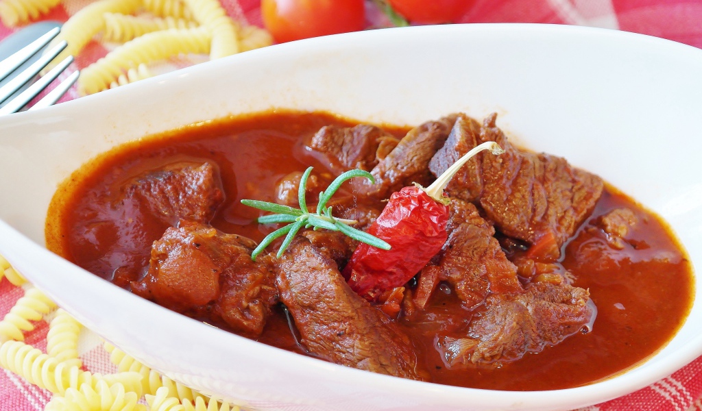 Мясной гуляш в белой тарелке с острым перцем