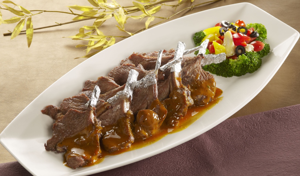 Мясо на белой тарелке с соусом и овощами 