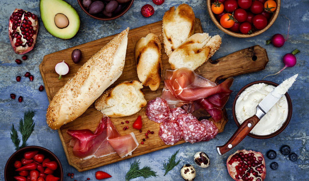 Мясные продукты с батоном и овощами на столе