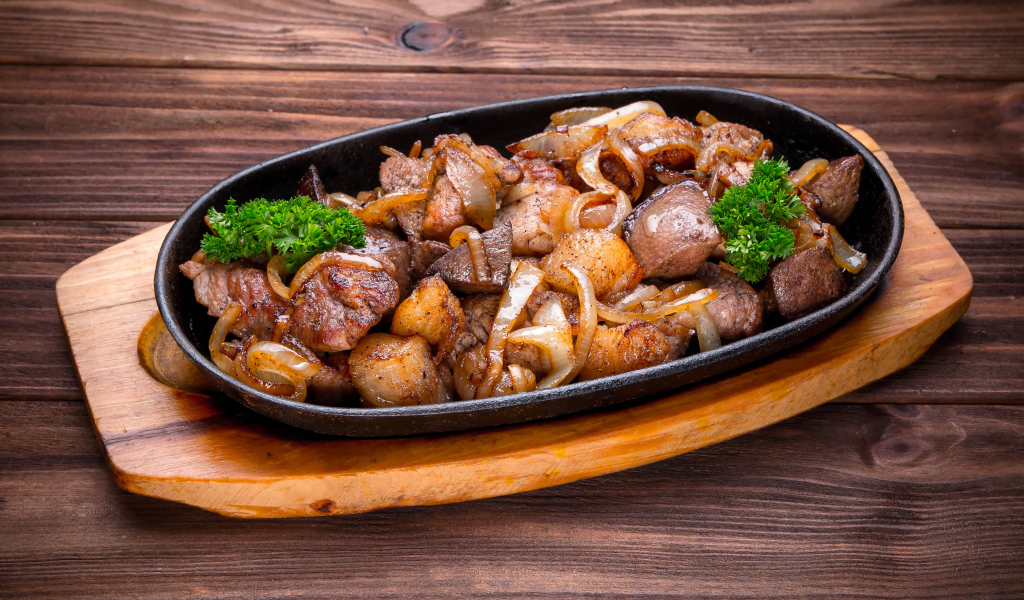Кусочки шашлыка с луком и петрушкой в сковороде