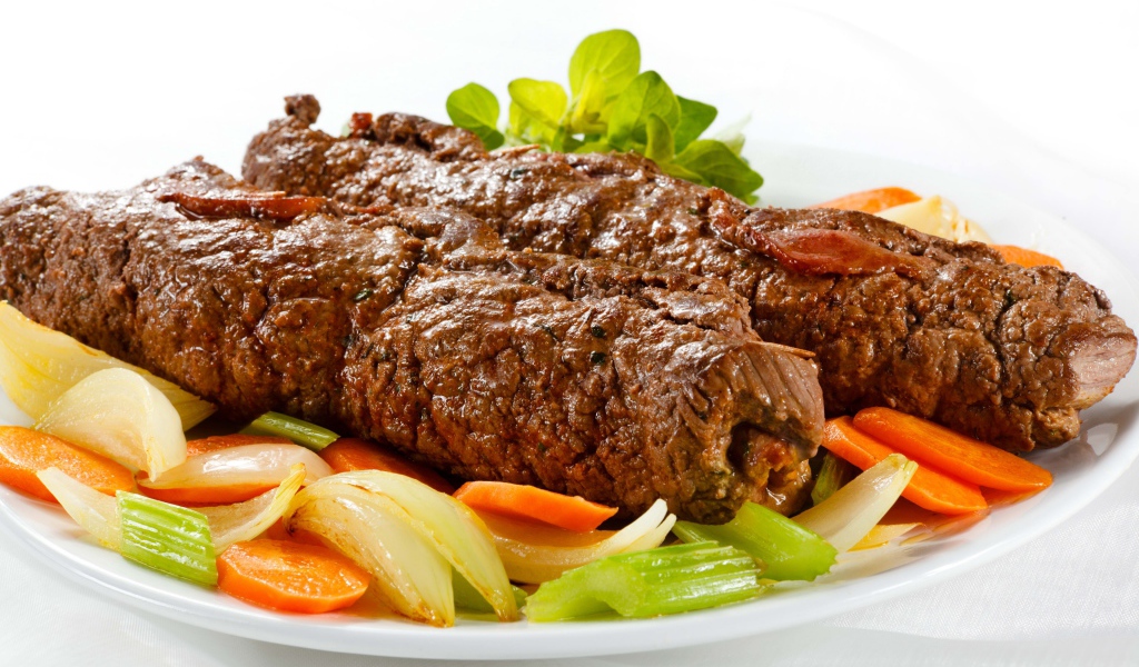 Свинина на тарелке с овощами на белом фоне