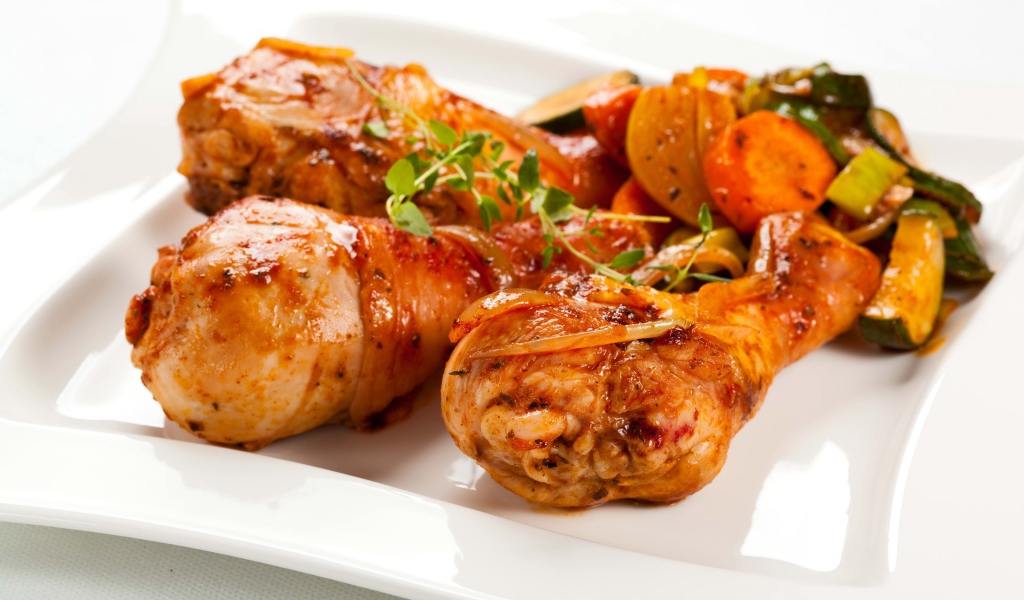 Жареные куриные ножки с овощами на белом фоне